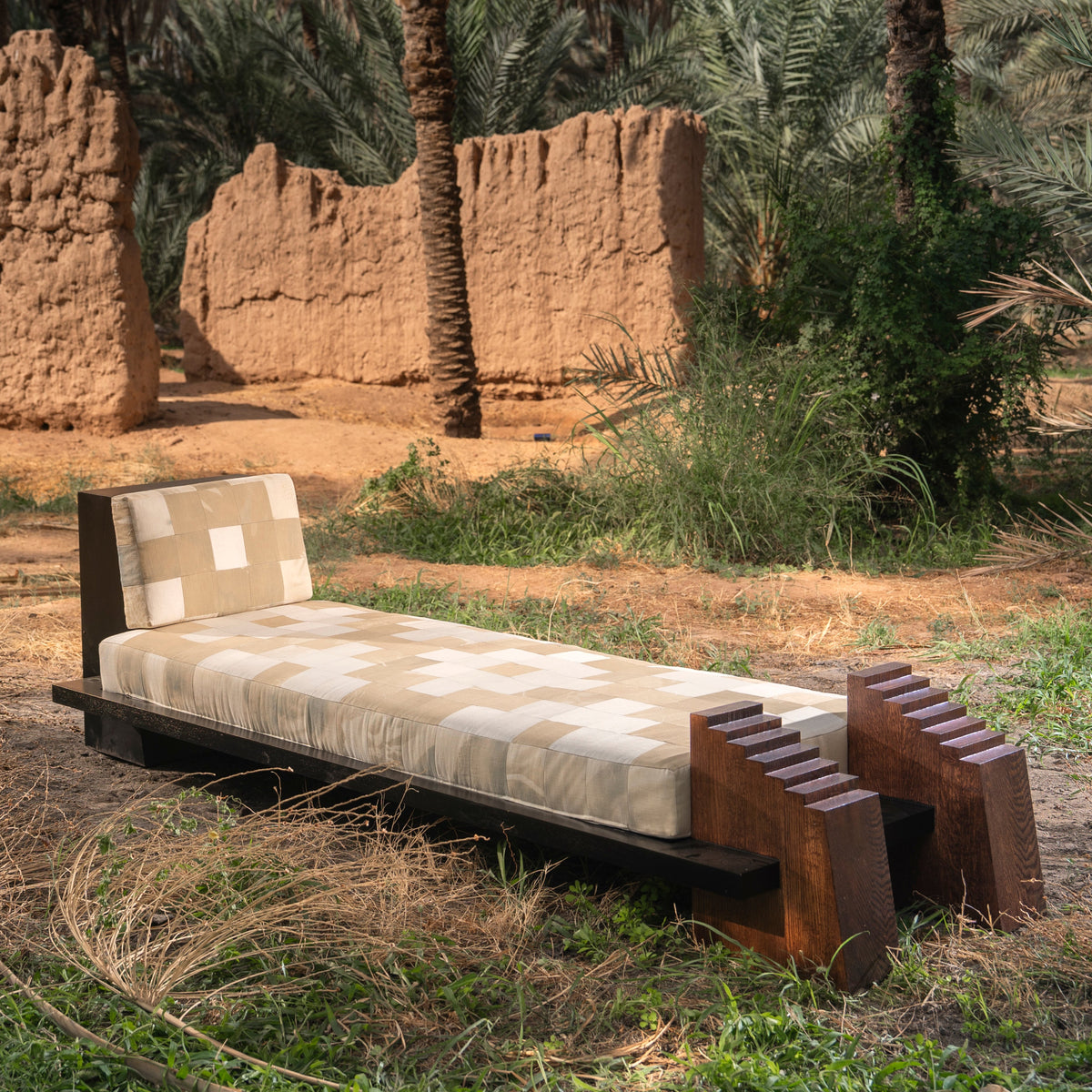 Dunan Dalan, lit de repos en bois et patchwork de textiles, devant des murs en terre à AlUla