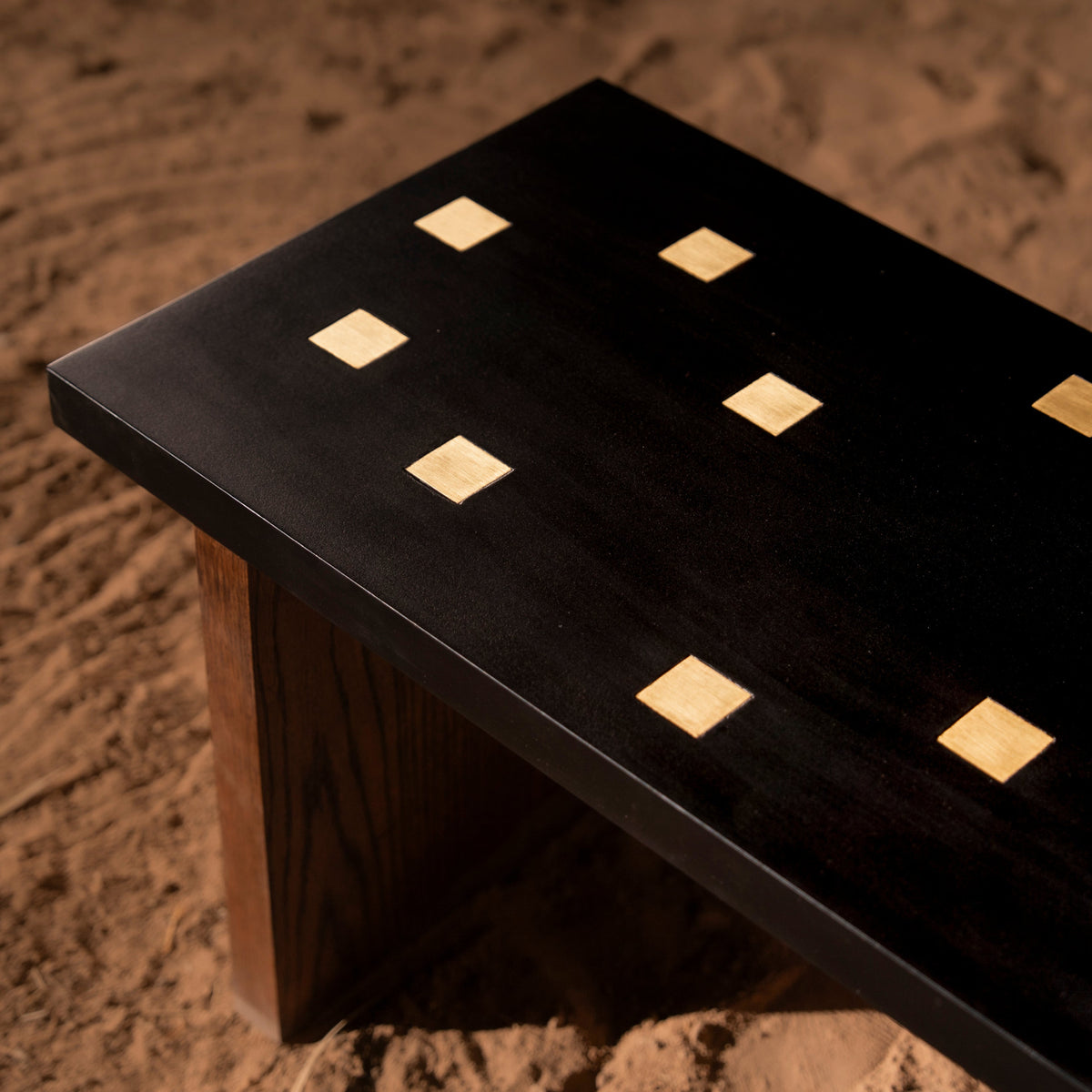 Détail d'un banc Sira Ladi : plateau noir incrusté de carrés de laiton, piètement en bois