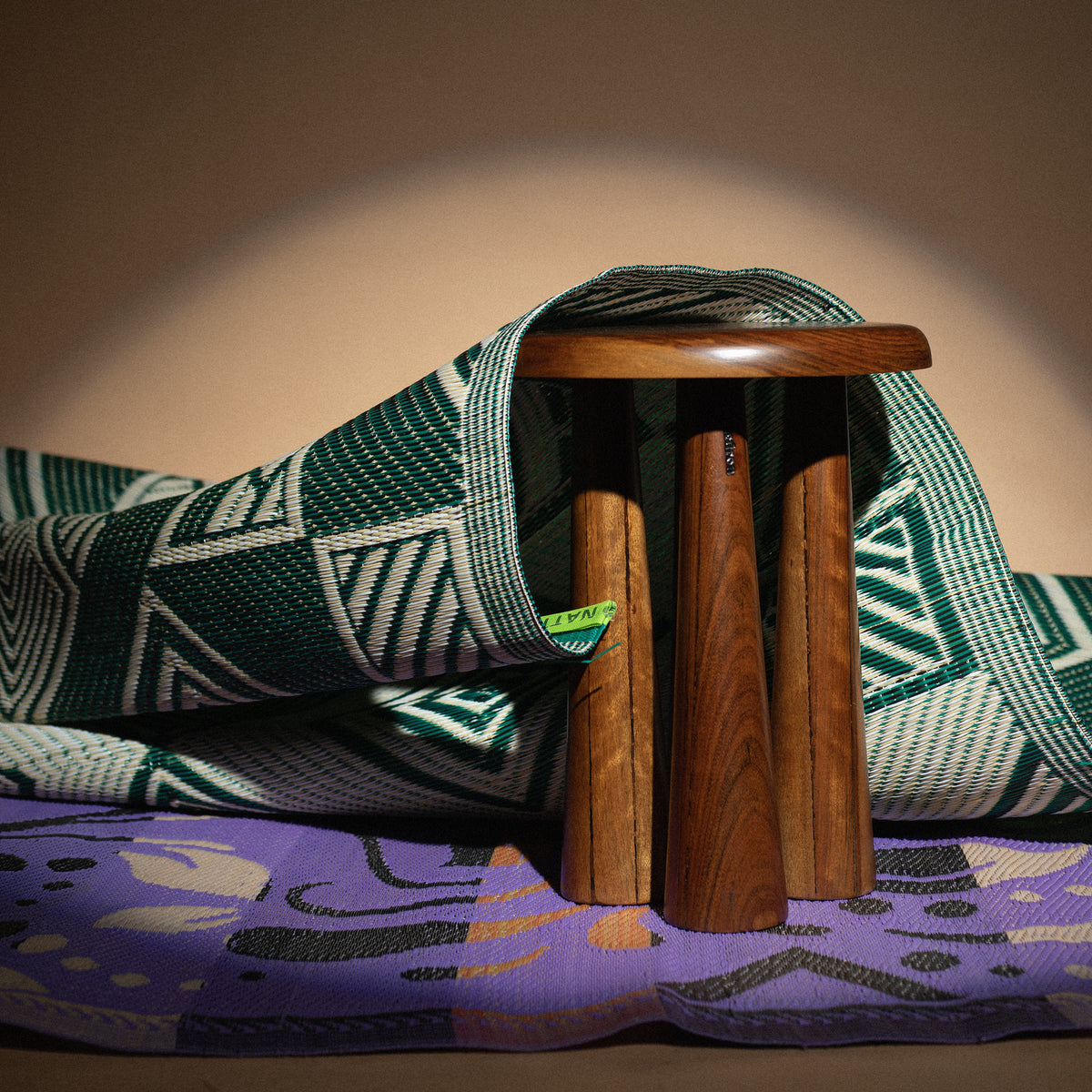 Tabouret Sédjan en bois posé sur des tapis tissés aux motifs verts et violets