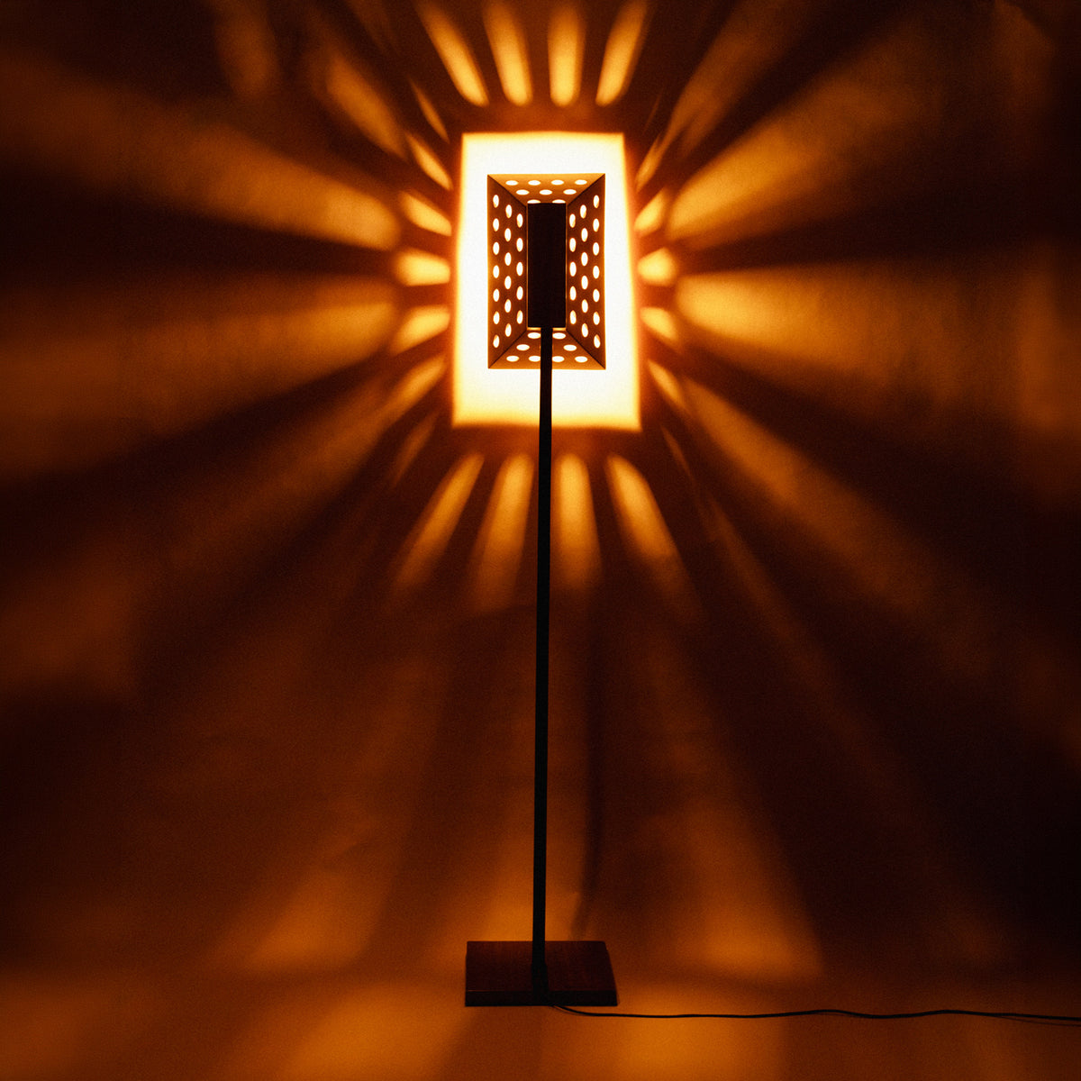 Lampadaire Oko allumé dans le noir, projetant des rayons de lumière sur le mur