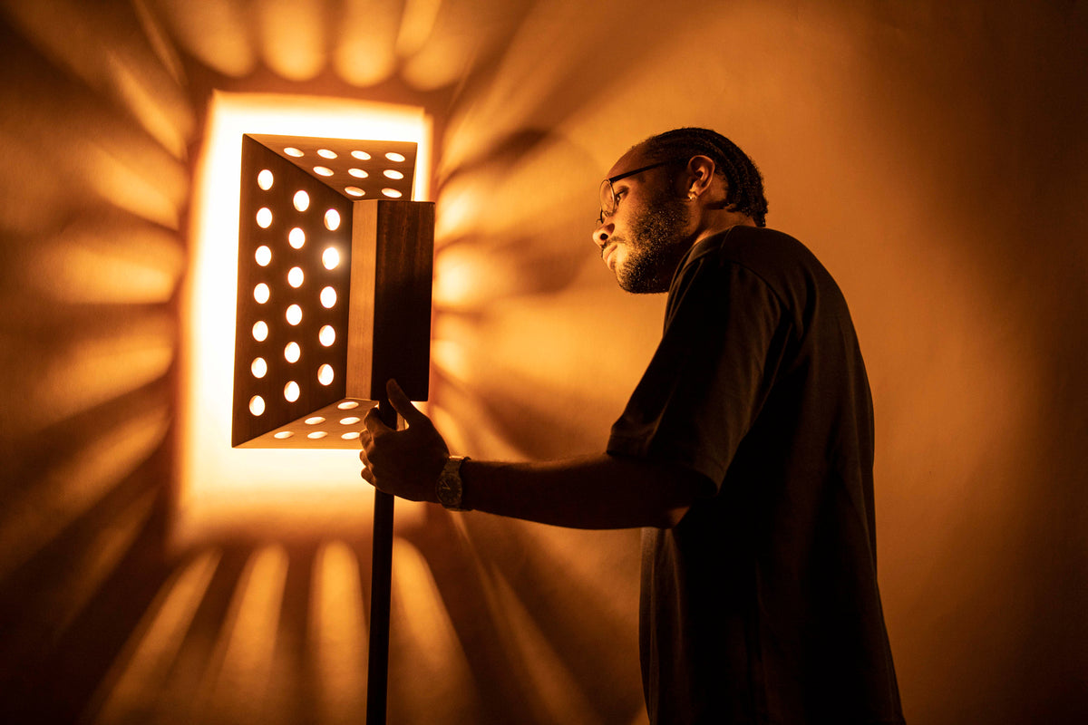 Lampadaire Oko en bois de Yundé allumé, projetant des rayons de lumière sur le mur